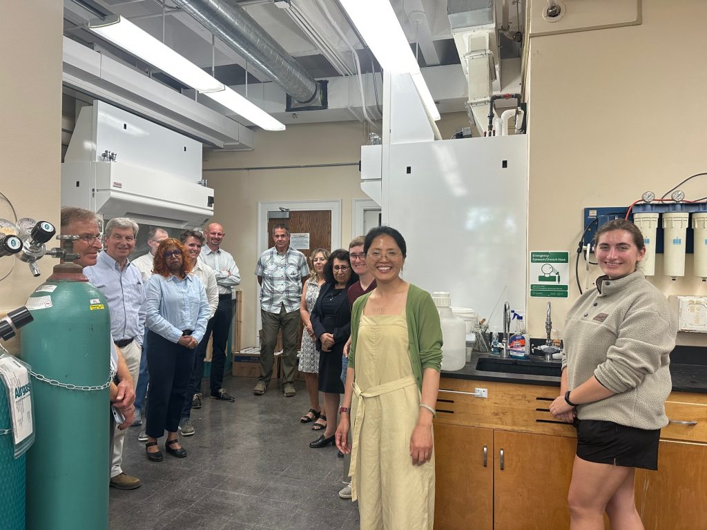 Approximately a dozen soil scientists are pictured smiling at the camera in the lab after a tour.